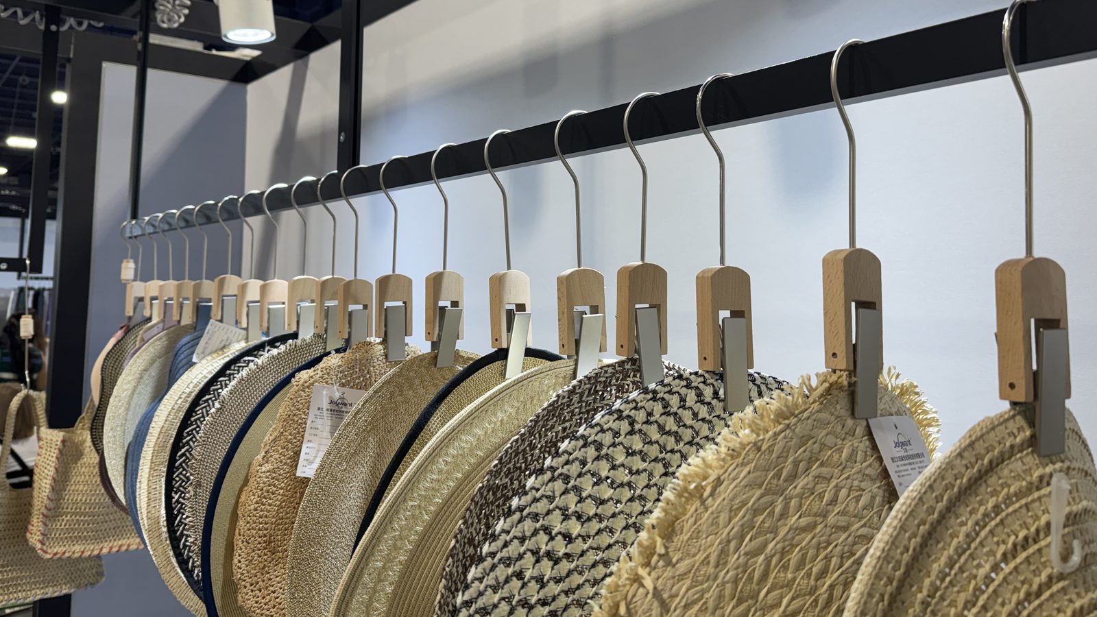 A row of straw hats on wooden clip hangers along a black rail at our Sourcing at MAGIC booth, Las Vegas 2026.