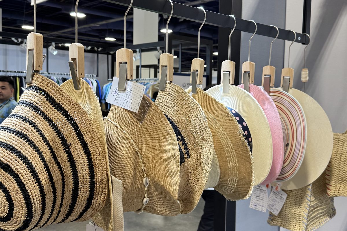 Close-up of straw hats on wooden clip hooks: striped braid, ribbon trim and a pale pink wide brim.