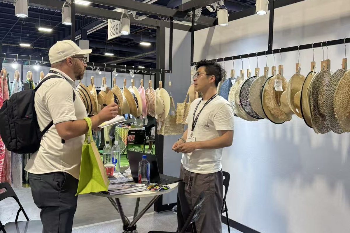 A visiting buyer and one of our team talking inside the booth, beside the hat rail and a small round table.